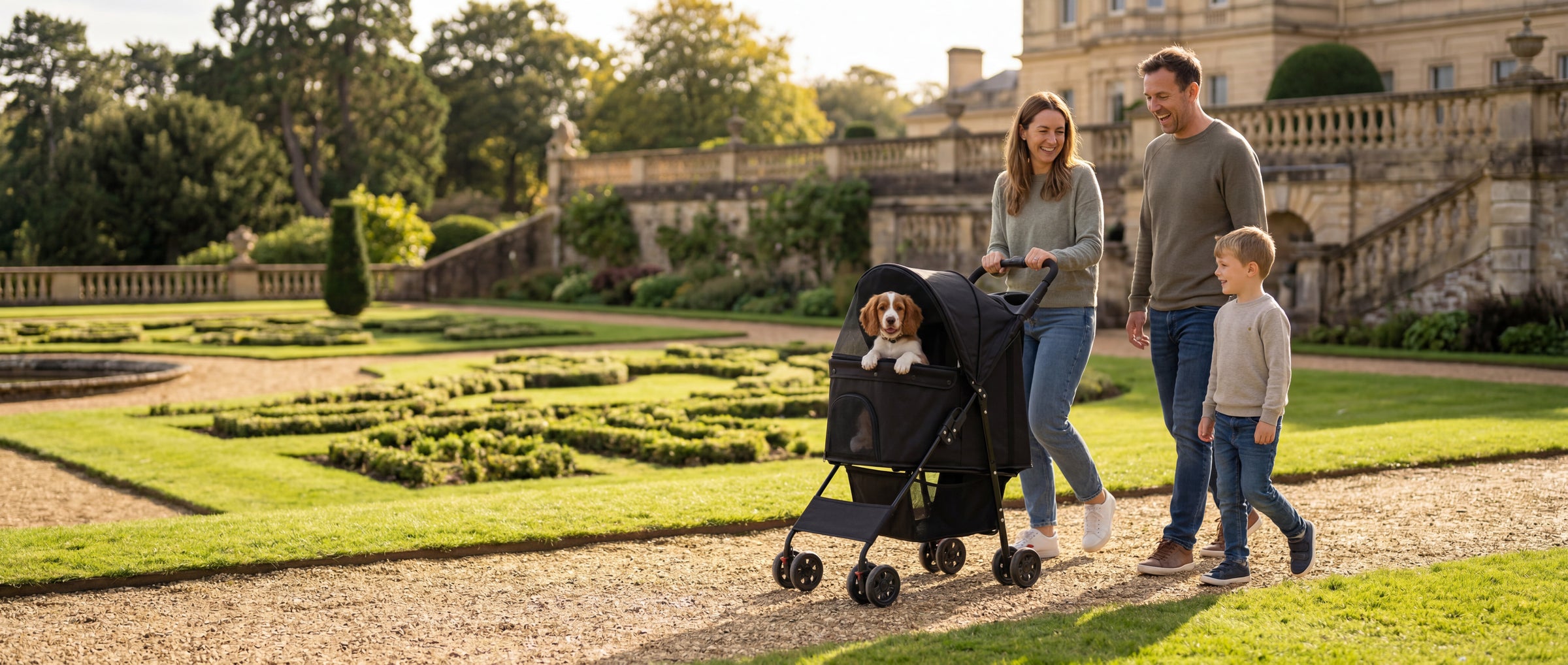 Family walking a dog in a pet stroller through park grounds with a large historic building behind them